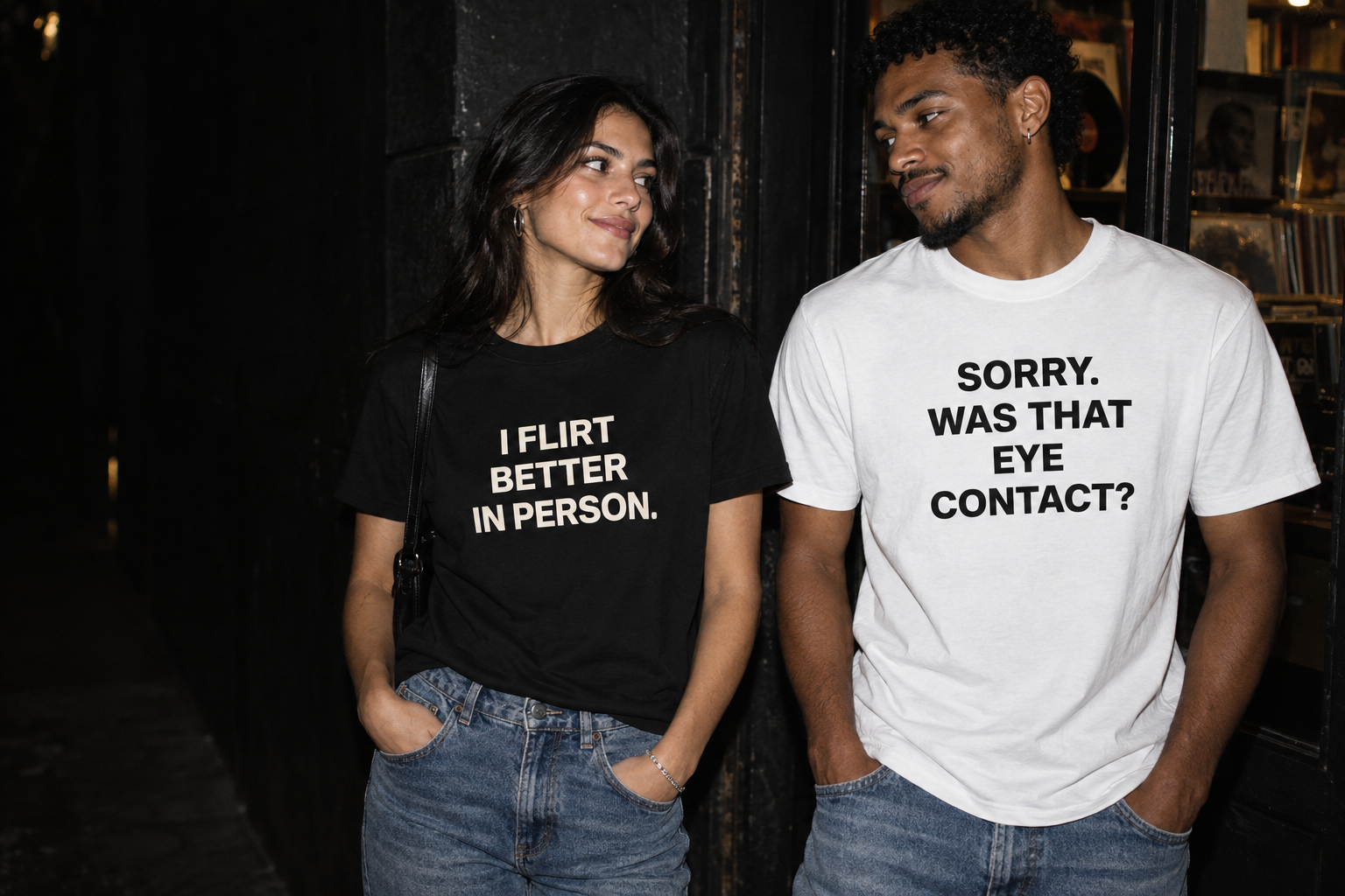 Two friends sharing a knowing glance in black and white Vuzelo statement tees on a city night.